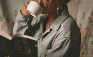 Black woman drinking from a coffee mug and reading