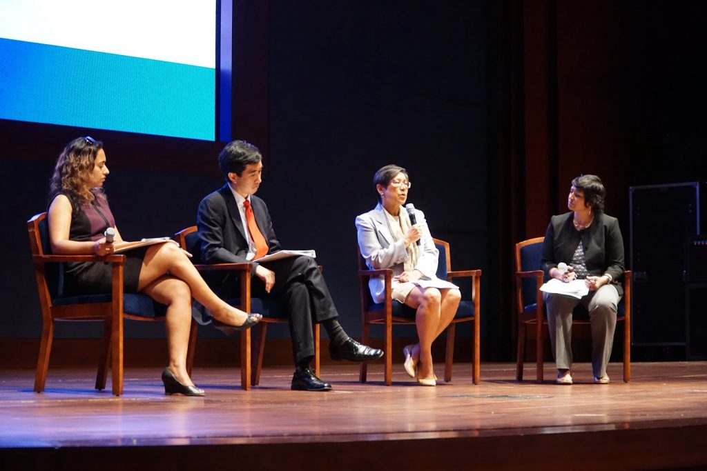 four people sit in chairs on a stage and one talks into a microphone