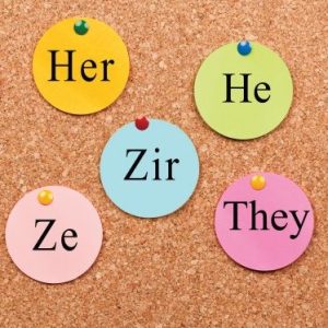 Cork board with various pronouns pinned to it on colored tags.